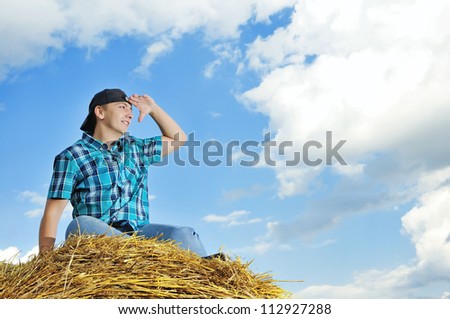 man on a stack of straw against a field and the sky
