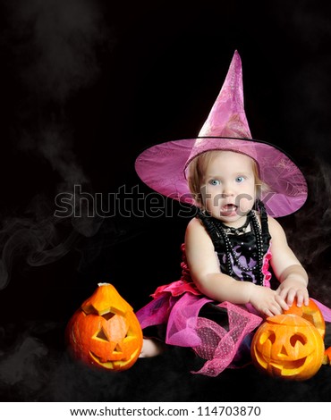Halloween little girl witch with a carved pumpkin over black background with smoke