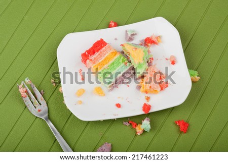 Messy leftover rainbow cake on a plate with crumbs around it