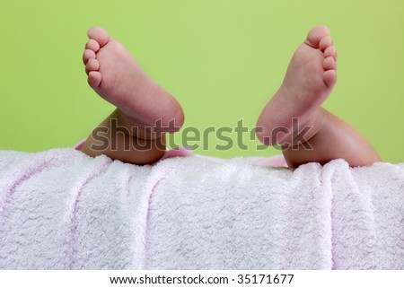 Pair of baby feet dangling on pink towel against green background