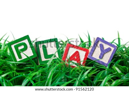 Alphabet blocks forming PLAY on a patch of grass