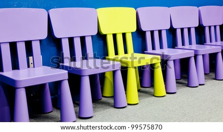 A yellow colored one in the middle of several purple colored chairs for children