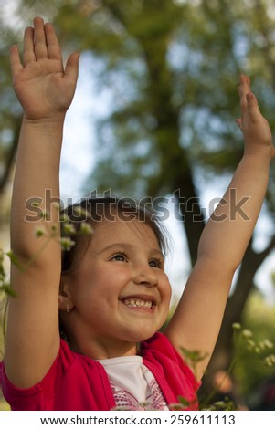 Happy little girl outside rising hands and smiling, beautiful facial expression