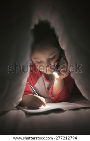 Girl reading and writing under the covers using flashlight