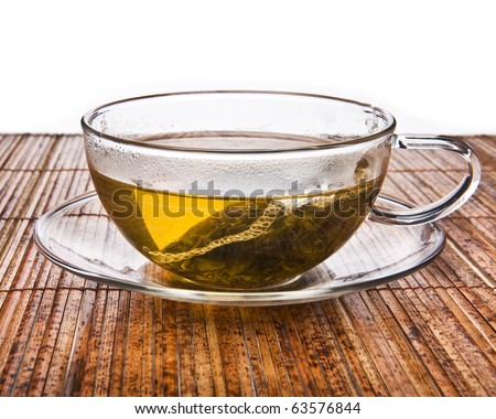 A cup of green tea with tea bag on a straw placemat, side view