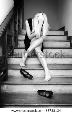 Sad girl is sitting on the stairs with her head bowed down