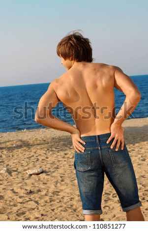 Resting handsome muscular man in jeans on beach