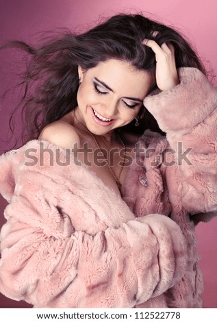 Beautiful happy smiling woman in a fur coat over pink