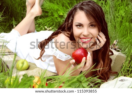 Happy Smiling Young Woman Eating  Apple in the Orchard. Basket of Apples.