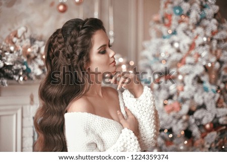Christmas portrait of attractive woman with wedding hairstyle. Beutiful brunette girl with long hair style wears in warm white woolen sweater over Christmas tree and xmas decorations.
