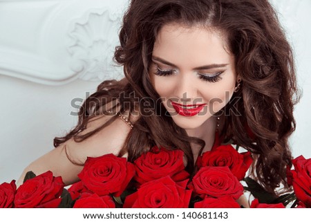 Closeup portrait of beautiful woman with curly hair and fashion makeup with red roses. Eyelashes. Eye shadows.