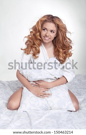 Beauty girl with curly hair embracing white pillow, happy smiling teen on bed, good morning.