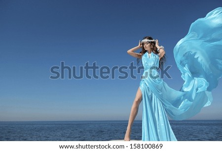 Luxury life. Fashion model girl with blowing tissue dress over blue sky, outdoors.
