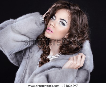 Beautiful brunette with makeup and wavy hair posing in mink fur coat isolated on black background
