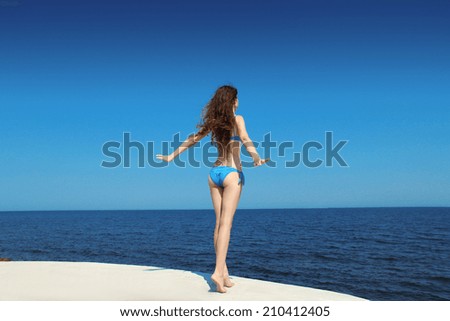 Enjoyment. Free brunette model woman in bikini over blue sky, outdoors. Brunette girl relax on the beach.