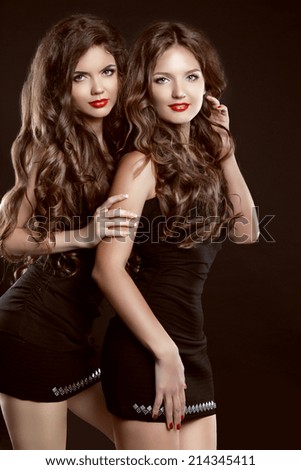 Beautiful two Young women with long healthy wavy hair styling and red lips posing in dress isolated on black background
