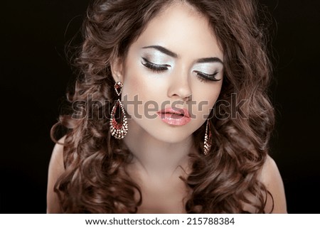 Beautiful fashion woman with makeup, long wavy hair and earrings isolated on black background.