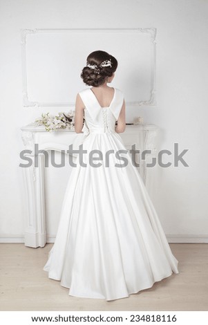 Bridal hairstyle. Beautiful charming bride in wedding luxurious dress posing against a white modern wall