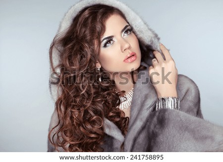 Fashion beautiful woman posing in fur coat. Winter Girl Model in Luxury clothes and furry hood Isolated on gray background.