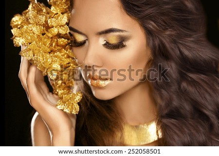 Golden makeup eyes closeup. Beautiful young woman in gold with flowers isolated on black background. Long brown hair.