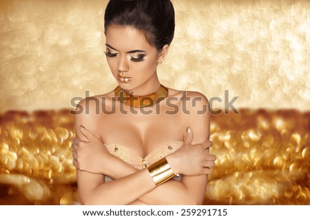 Makeup. Fashion glamour girl model in luxurious golden jewelry over holiday bokeh background. Beautiful brunette woman posing.