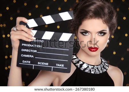 Beautiful brunette woman model holding film clap board cinema. Fashion portrait of girl with makeup, hairstyle and expensive jewelry.