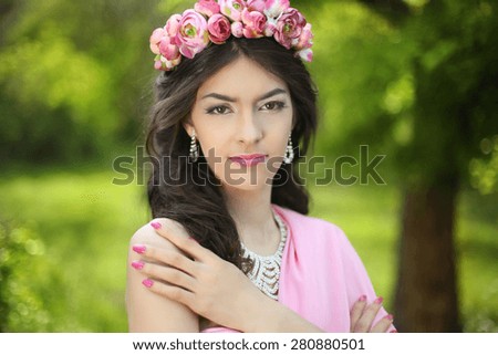 Brunette girl with flower chaplet in green filed wearing in pink dress on green field.