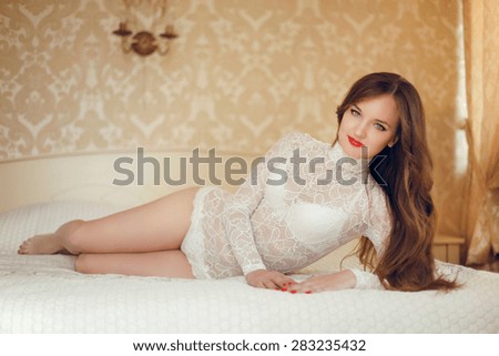 Beauty bride portrait of young beautiful sexy woman with long wavy hair. Pretty girl lying on the bed in white lingerie in luxury interior. Alluring.