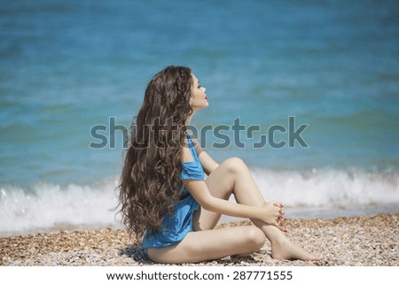 Young brunette girl enjoying and sunbathing on the beach with long wavy hair in blue bikini