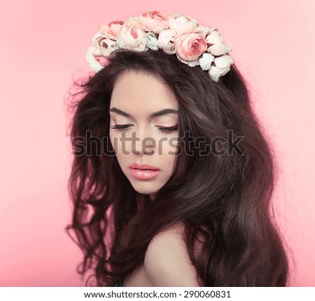 Makeup. Beautiful girl with long wavy hair and flowers chaplet on head. Attractive young woman model isolated on pink background.