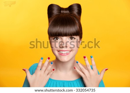 Happy smiling teen girl with bow hairstyle and colourful manicured polish nails. Funny girl showing ten fingers isolated on studio yellow background.