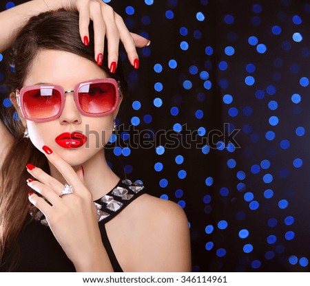 Beauty. manicured nails. Fashion model girl in sunglasses with bright makeup, luxurious jewelry over  on blue lights background.