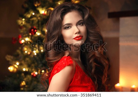 Christmas Santa. Beautiful smiling woman model. Makeup. Healthy long hair style. Elegant lady in red dress over christmas tree lights background. happy new year.