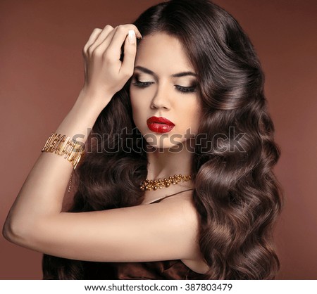 Healthy hair. Makeup. Beautiful brunette girl with long wavy hairstyle. Red lips. Elegant lady with jewelry.