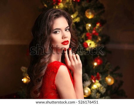 Christmas. Beautiful smiling woman. Manicure nails. Makeup. Healthy long hair style. Elegant lady in red dress over christmas tree lights background. happy new year.