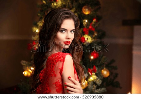 Christmas. Beautiful smiling woman. Manicure nails. Makeup. Healthy long hair style. Elegant lady in red dress over christmas tree lights background. happy new year.
