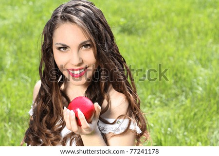 Beautiful young woman with red lips and long hair present red apple on the nature background
