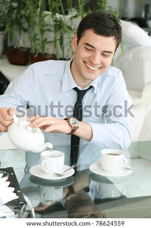 Smiling young men pours tea into a cup. Beautiful smile. Coffee time