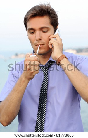 Young businessman with telephone,handsome man smoking cigarette, outdoors