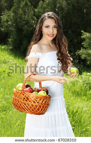 Smiling Female presents basket of apples over nature