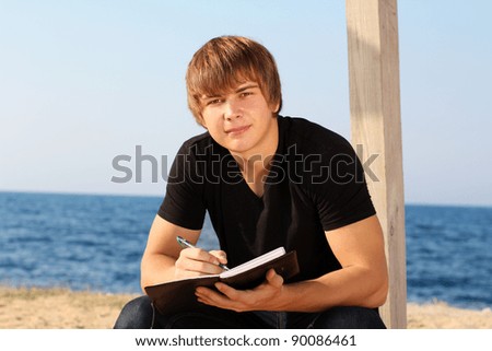 Attractive young man with writing pad on the beach