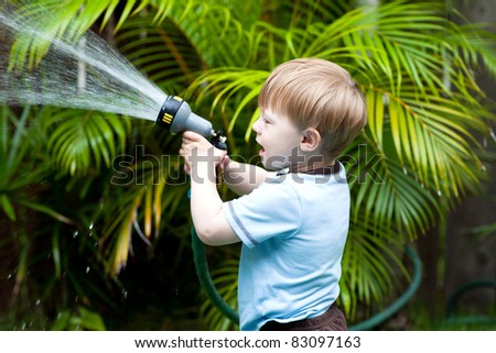 Adorable toddler watering plants in the back-yard
