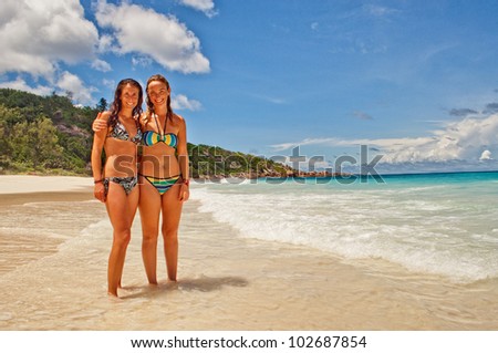 Two female friends on tropical island beach vacation  in the warm sunny Seychelles island oceans and palm trees