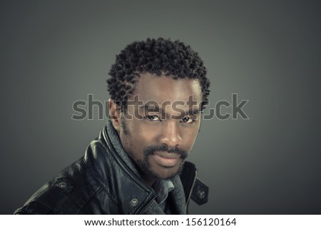 Fashion portrait of handsome, stylish, young african man isolated on grey background with leather jacket