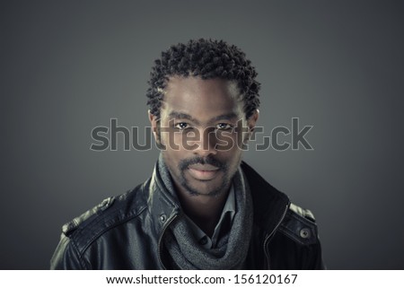 Fashion portrait of handsome, stylish, young african man isolated on grey background with leather jacket