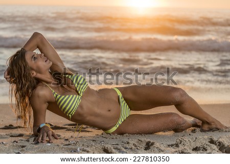 Female swimsuit model at the beach with blue sky and sand around during sunset