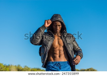 Fit, athletic and muscular African black male wearing black bomber jacket hoodie with zipper, isolated with blue sky