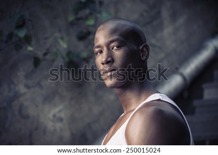 Sad black, african american man, thinking against a concrete wall, wearing vest shirt