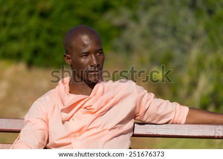 African black man sitting on wooden park bench, relaxing and stretching as he thinks
