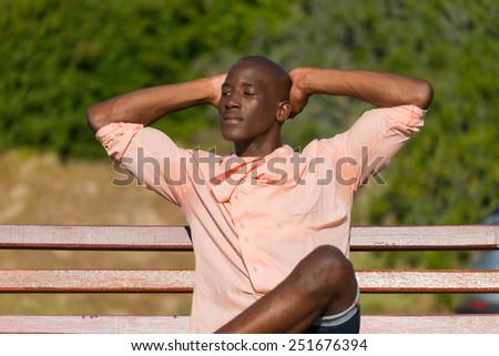 African black man sitting on wooden park bench, relaxing and stretching as he thinks